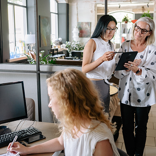 Illustrasjonsfoto av dame som sitter foran PC og to damer som ser på nettbrett. Foto: Pexels v. Yan Krukau