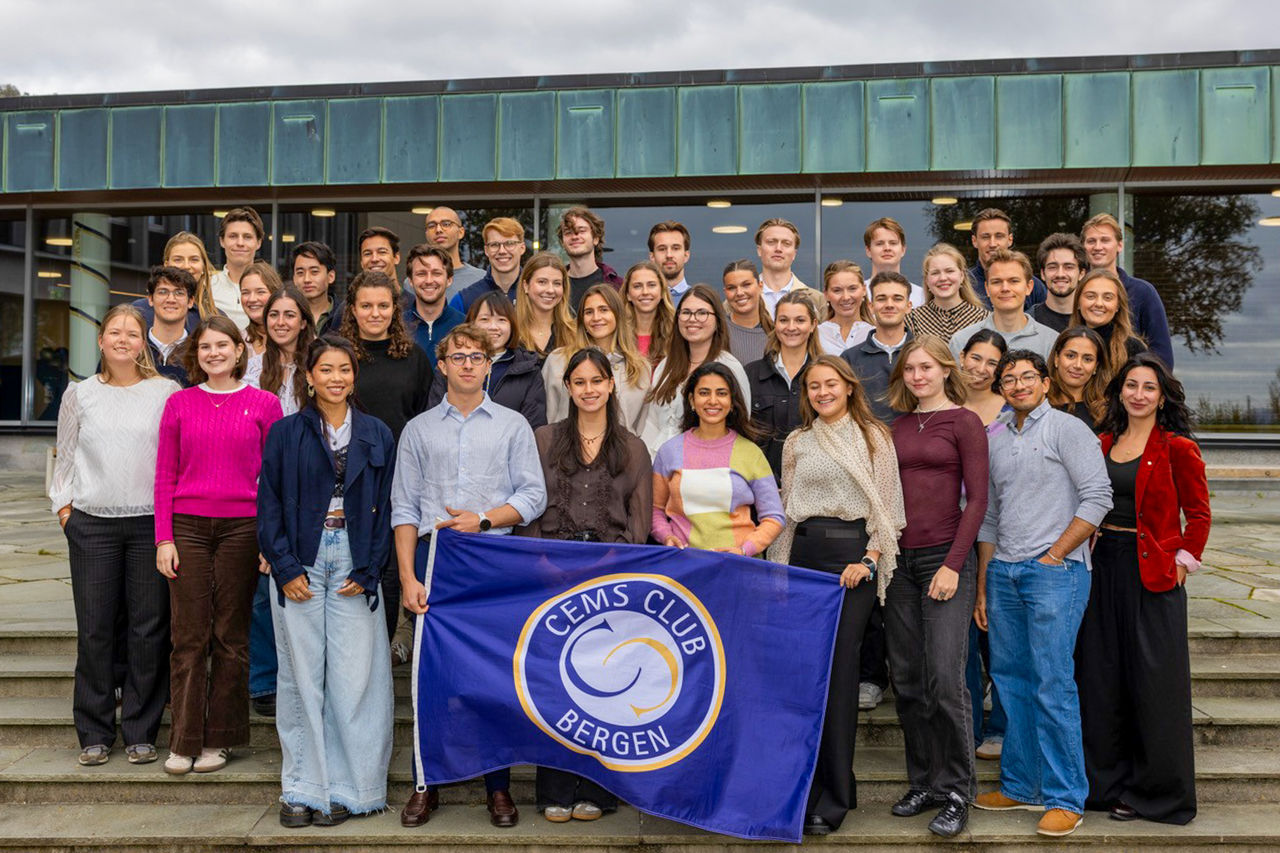 A group photo of the CEMS cohort at NHH during the fall 2026 semester. Some students on the front row are holding the CEMS flag.