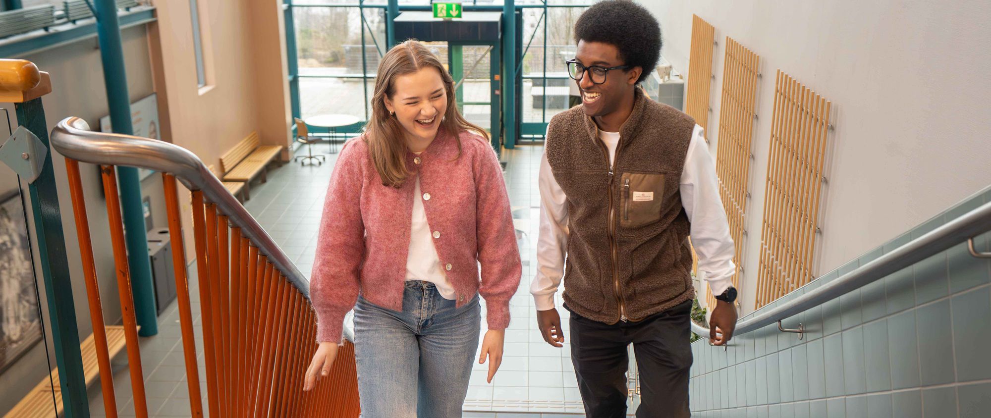 Two smiling students walking up a staircase at the Norwegian School of Economics (NHH).